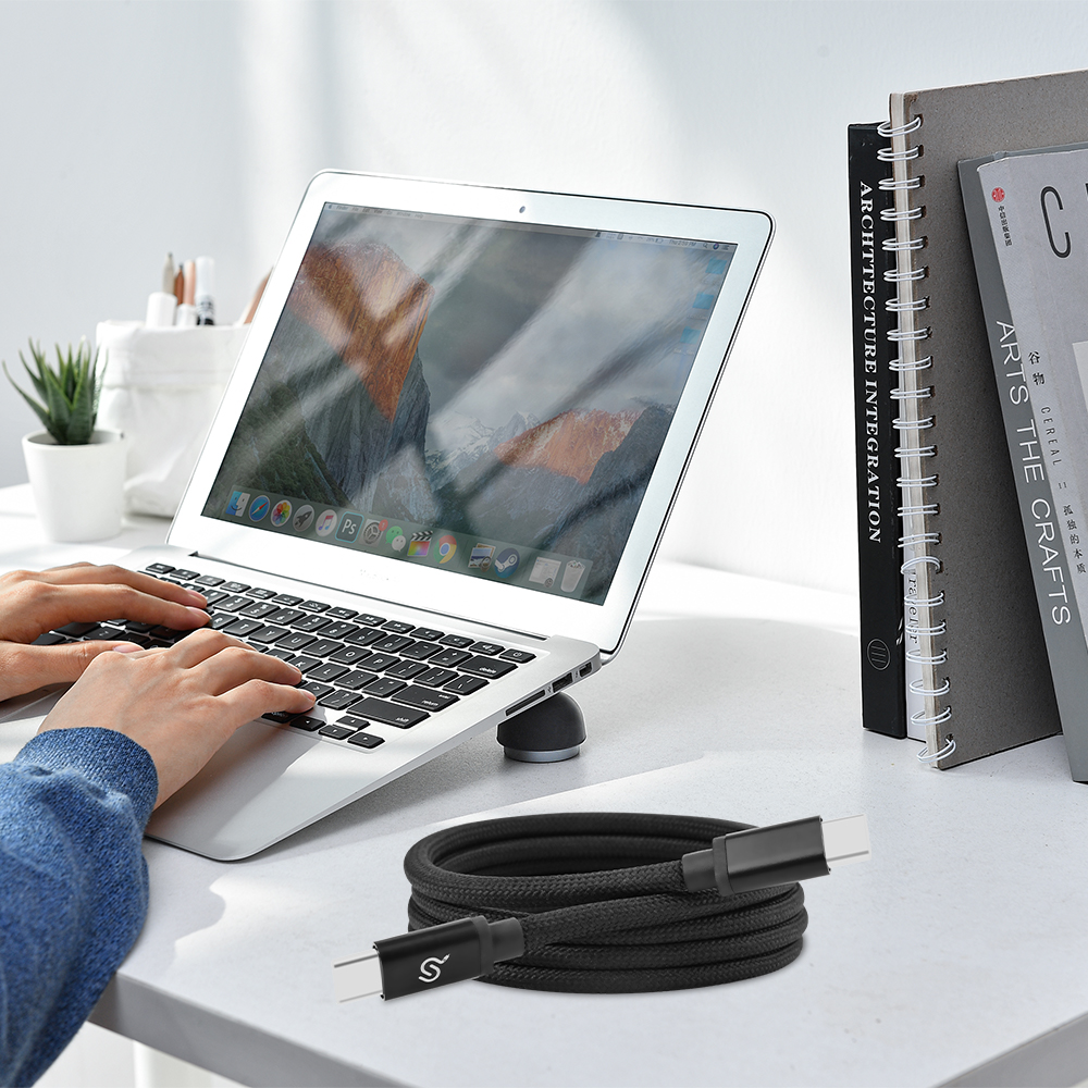 A black nylon braided USB-C magnetic charging cable neatly coiled near a laptop on a clean desk