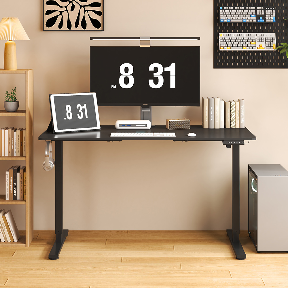 A height-adjustable standing desk frame is paired with a writing desk, on which a laptop, tablet, and some books are placed